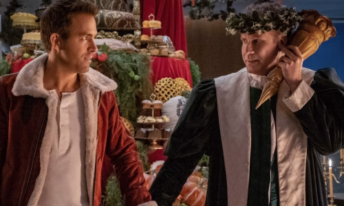 Ryan Reynolds wears a red jacket while holding hands with Will Ferrell, who is dressed like The Ghost of Christmas Present.