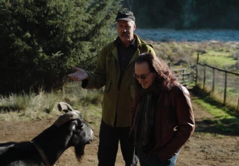 Two men talk to a goat on a ranch