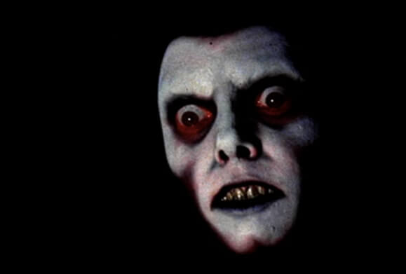 A pale demonic face scowls in the darkness.