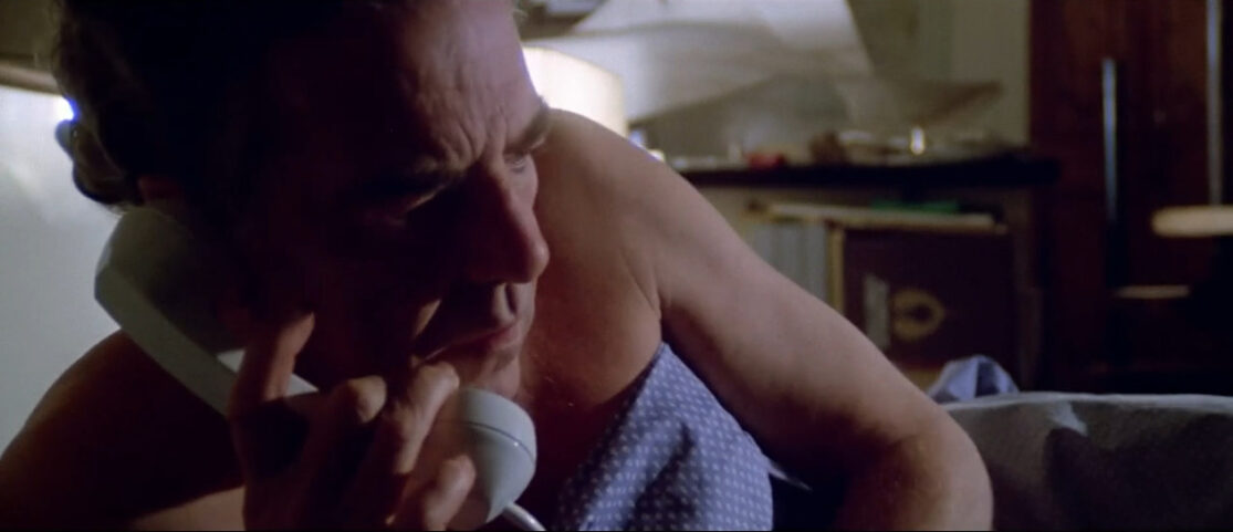 A man, in bed, answers a late-night call.