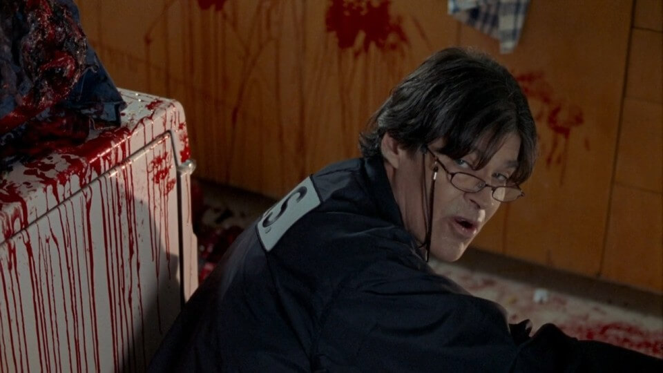 A coroner stoops near a corpse in a very bloody room.