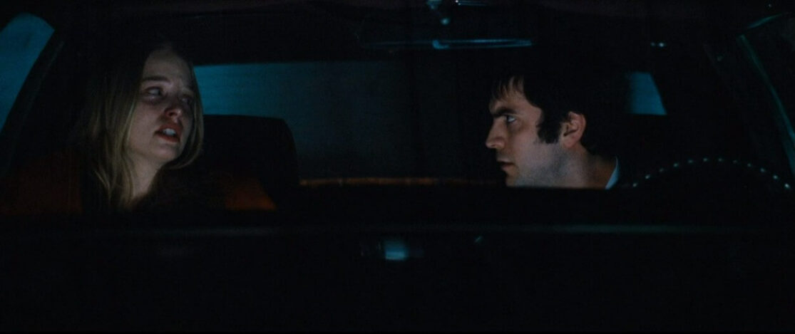 A terrified woman in a car with a serious looking man.