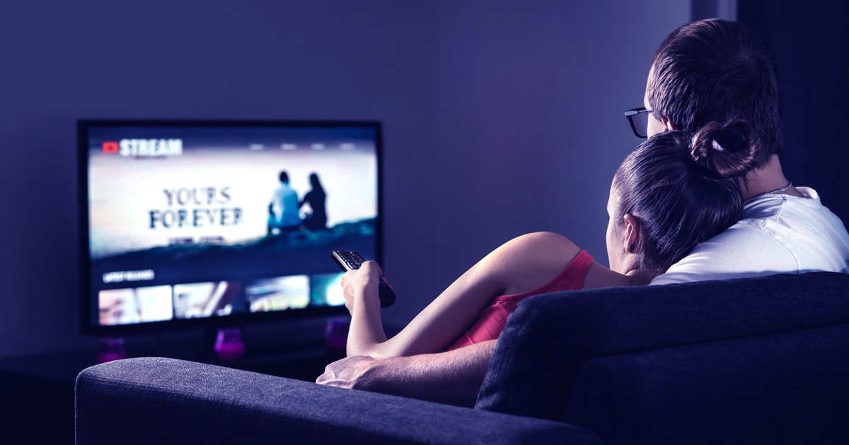 A couple sitting on a couch watching a streaming service.