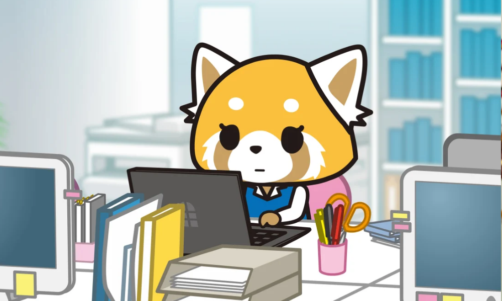 Aggretsuko1000x600 A cute yellow-colored red panda in business clothes sits in her office, looking at her laptop.