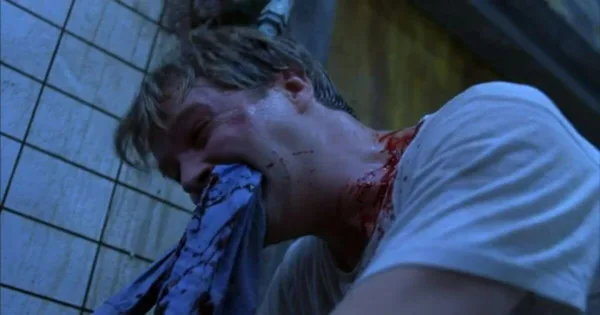 A scene from the first Saw movie showing a bloodied, frantic man chomping on a bloody shirt while (this part is not shown) sawing off his foot in an iconic sequence from the film.