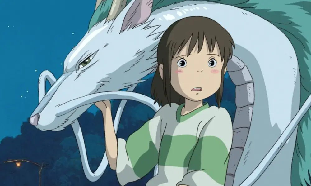 SpiritedAway1000x600 An animated girl with brown hair and a green striped shirt stands in front of an Asian-style white dragon.