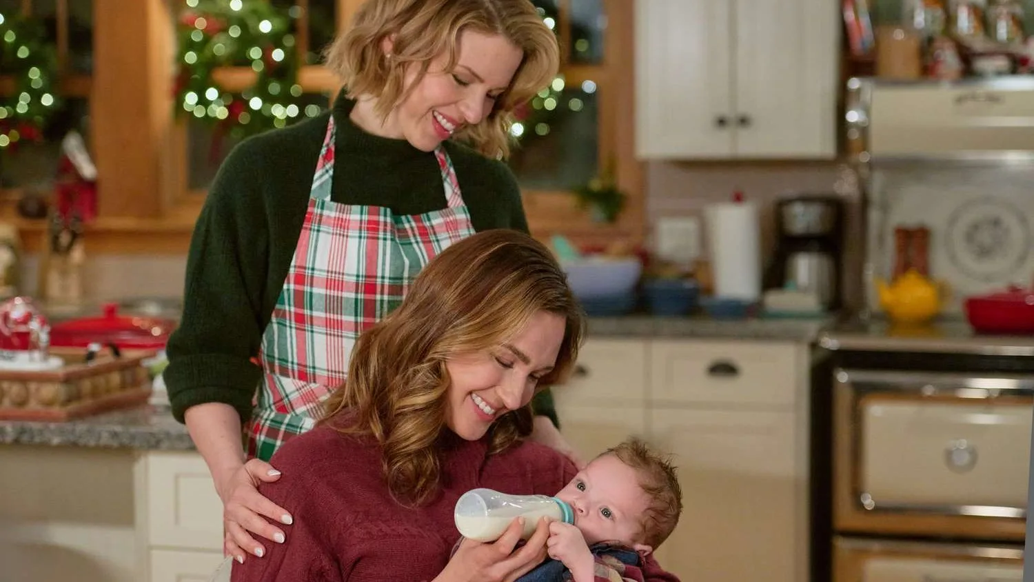 In a scene from the Hallmark Christmas movie The Christmas Baby, two women in a kitchen gaze lovingly at a new baby.