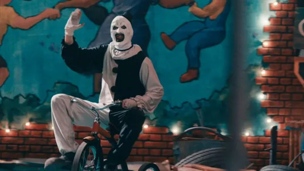 Image of a killer clown riding a tricycle in a circus tent. A scene from Terrifier 2, streaming now on Tubi.